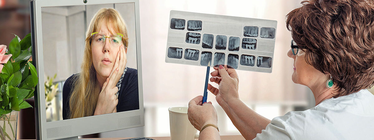 Young woman communicates with dentist in internet Mature female dentist examining young woman during internet video session. Virtual doctor in white uniform looks at x-ray image of teeth. Long haired blonde woman has a toothache. She suffers pain in monitor. Horizontal indoors shot on blurry office background