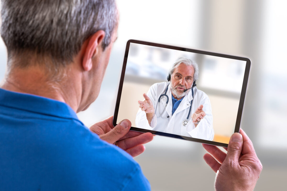 Virtual Visits with Telemed Remote consultation- Doctor sitting at hospital, with laptop, having an online call with patient showing tablet device